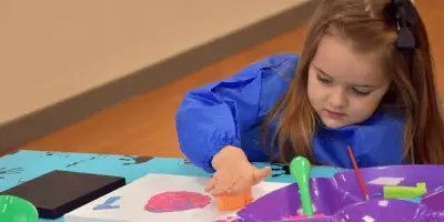 A girl pushing a painted sponge onto a canvas