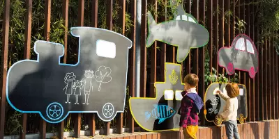 A boy outside drawing on vehicle shaped chalkboards