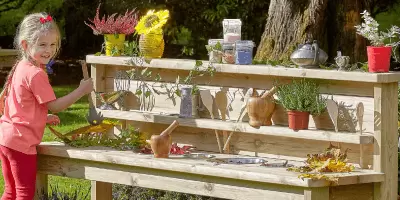 A girl outside in the sunshine playing with a mud kitchen