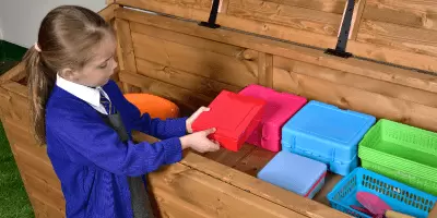 A girl in school uniform putting an item away into a big outdoor storage chest