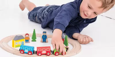 A boy laying on the floor playing with a wooden train set