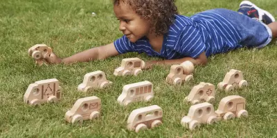 A boy laying on the grass playing with wooden cars